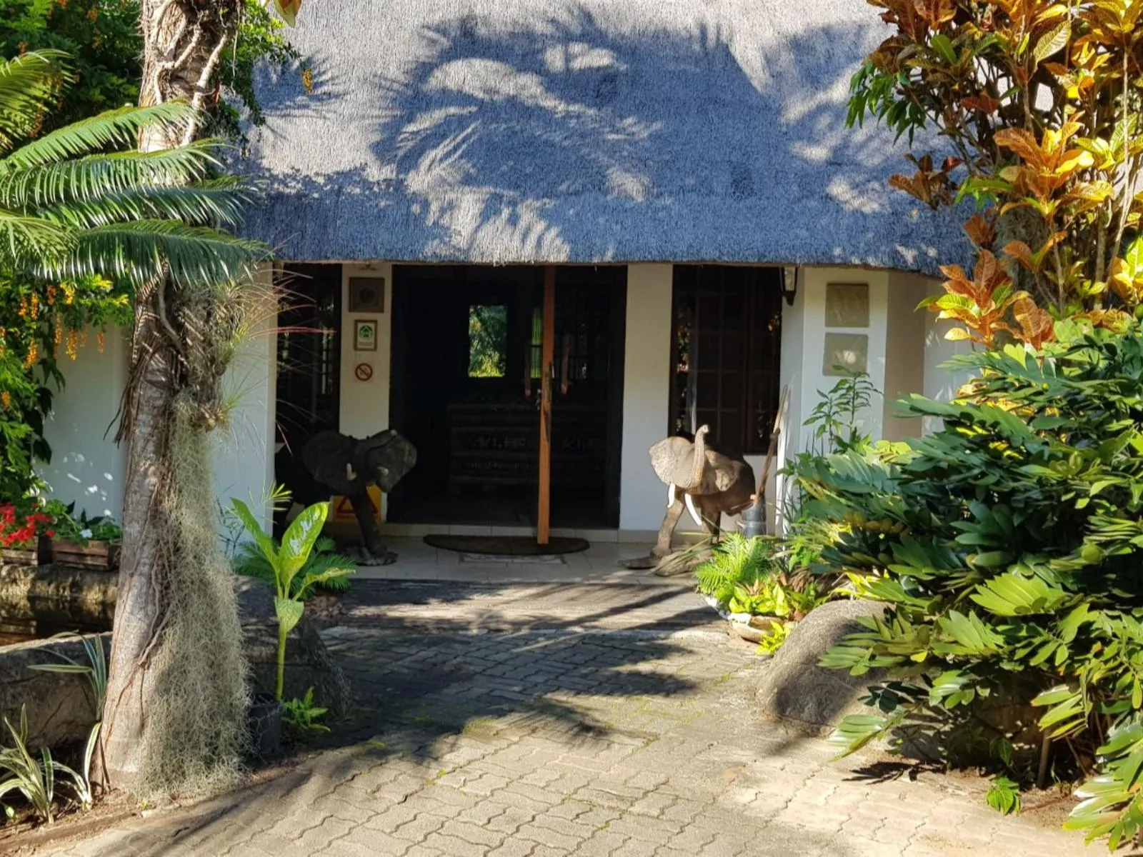 Entrance of a thatchedroof building with lush greenery and elephant statues