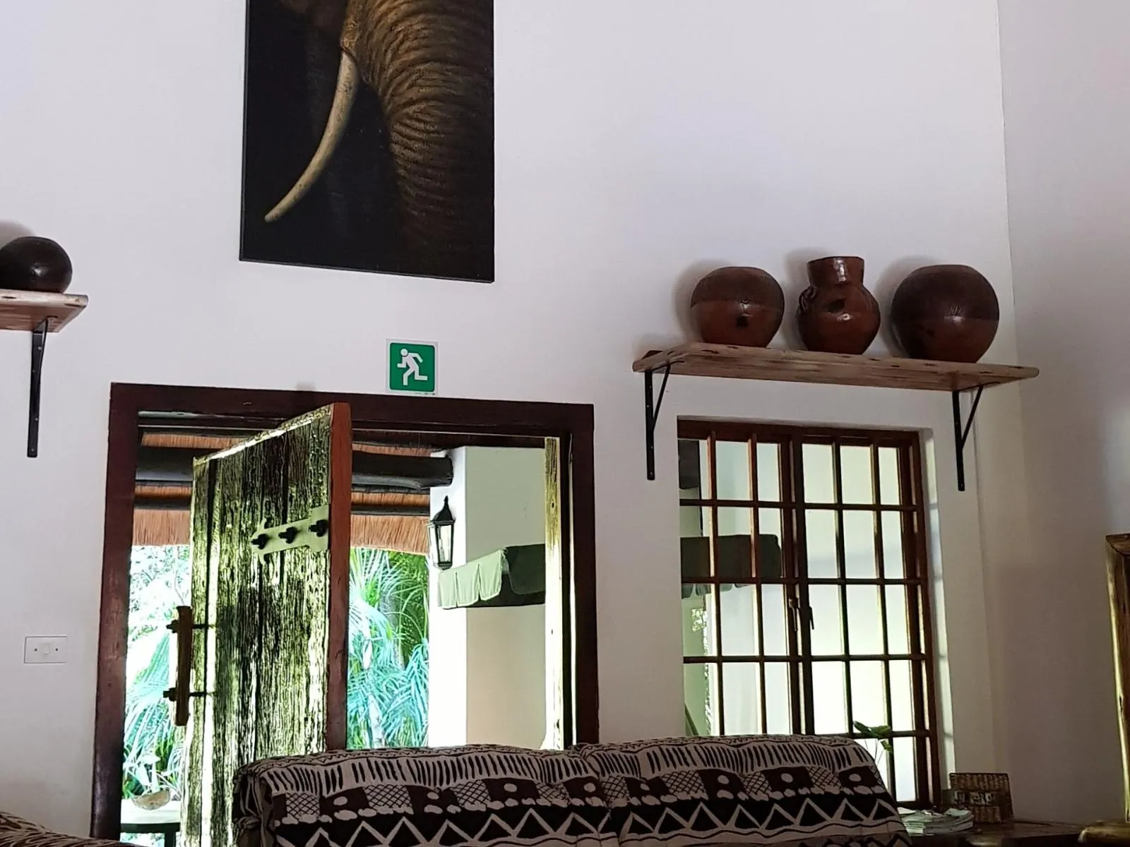 Painting of an elephant above a couch with African pottery on a shelf
