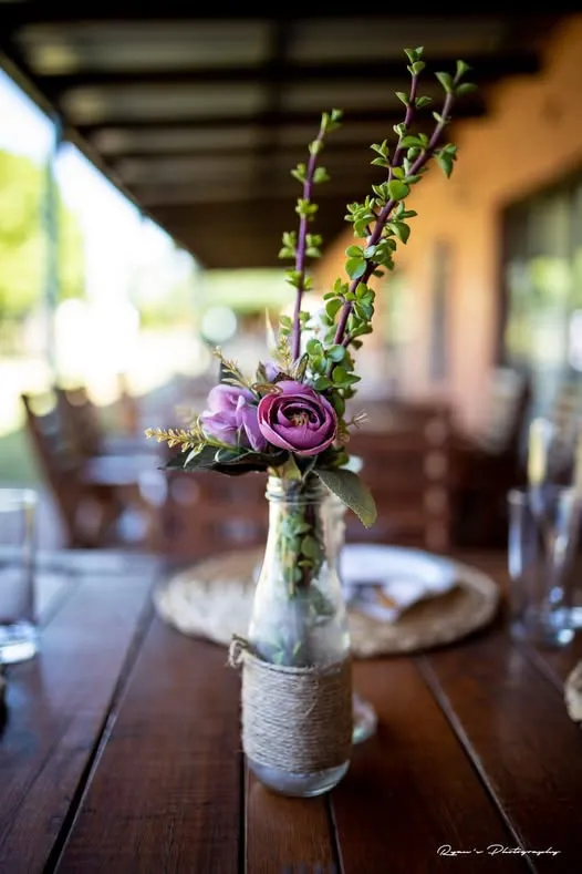 Purple flowers in a glass bottle on a wooden table in a restaurant
