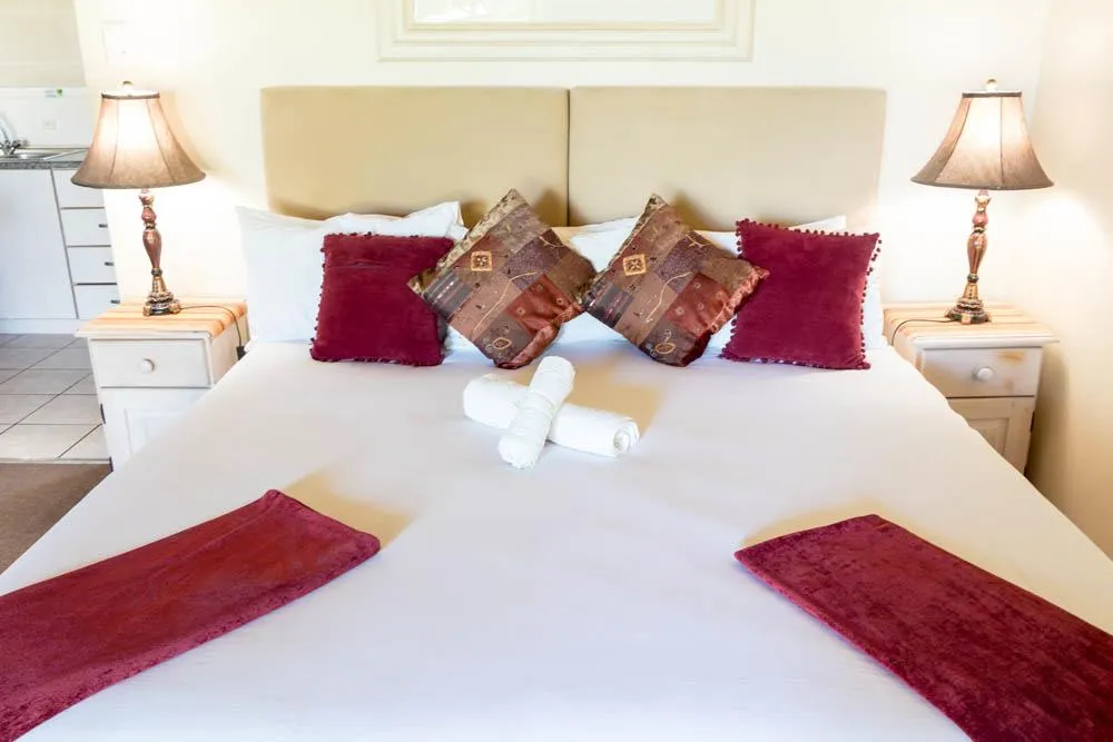 A neatly made bed with red and brown pillows and folded towels