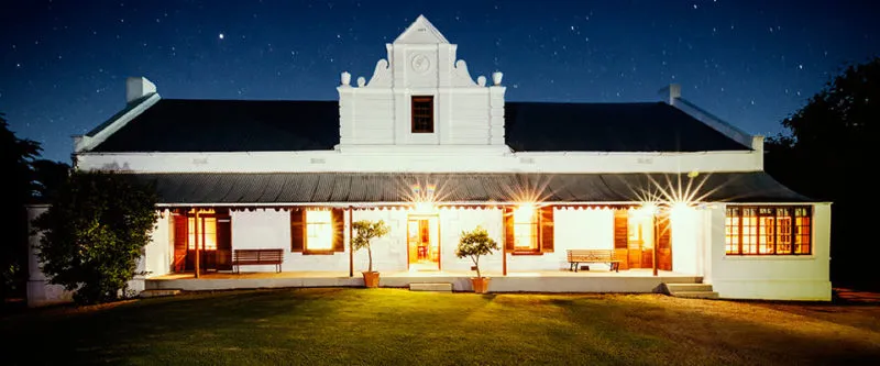 A welllit white colonialstyle house at night with a green lawn