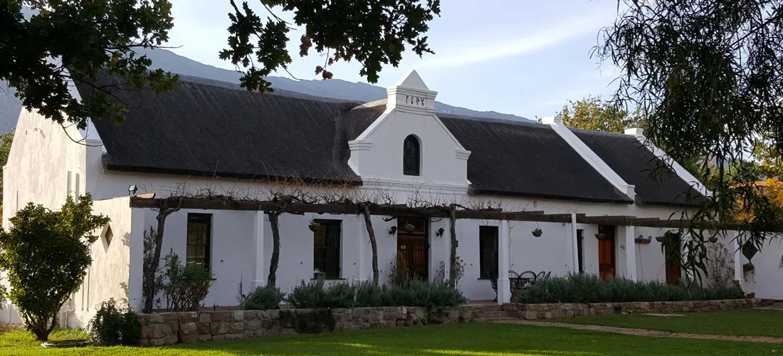 White Cape Dutch house with gabled facade and lush garden in front