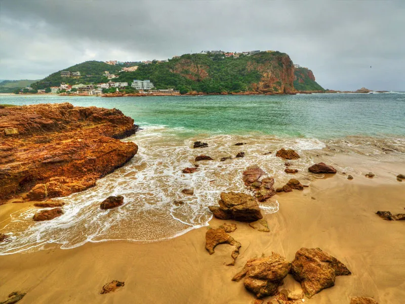 Rocky beach with waves green hills and buildings in the background