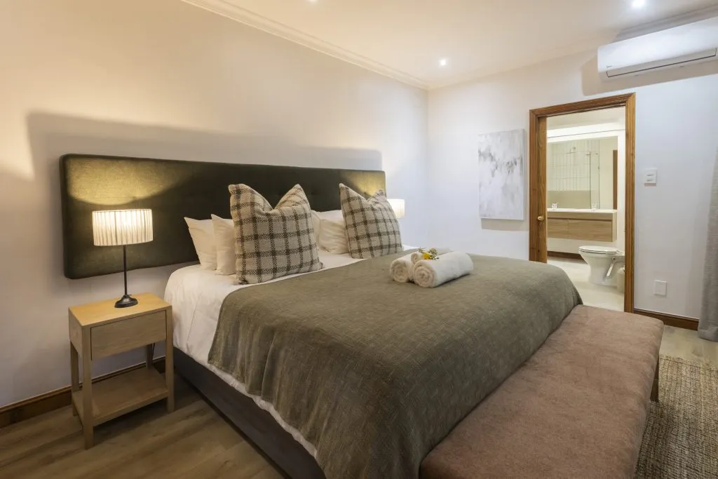Modern bedroom with a large bed and ensuite bathroom visible in the background