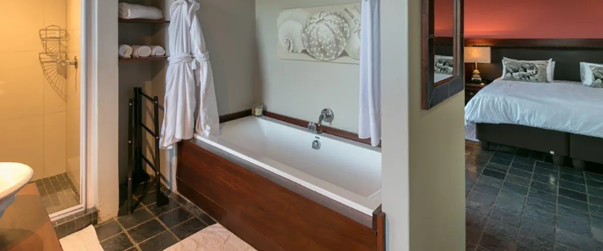 Bathroom with wooden bathtub robes and adjacent bedroom with double bed