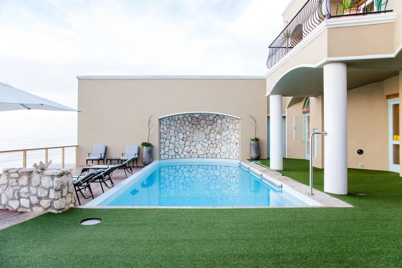 Modern pool area with lounge chairs stone wall and ocean view