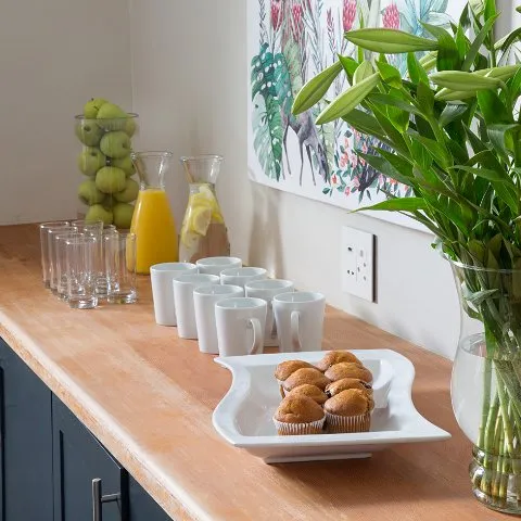 Wooden table with juice cups muffins and a plant in a vase