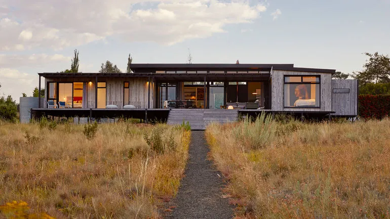 Modern house with large windows surrounded by tall grass in a rural setting