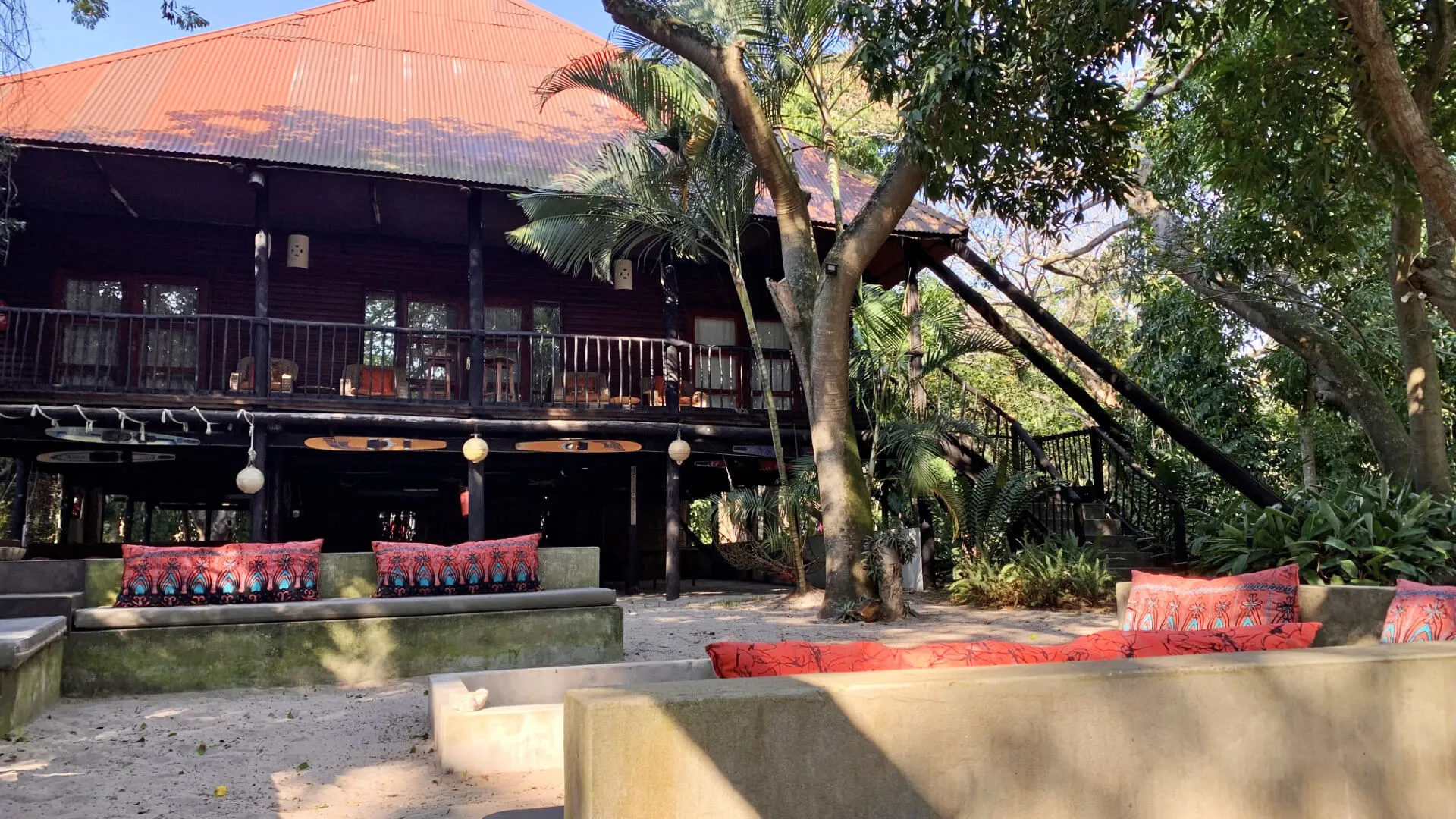 Wooden house with red roof and red cushions in a lush garden setting