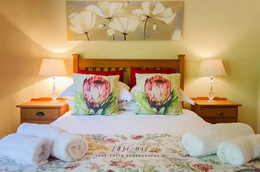 Bedroom with floral pillows white bedding and bedside lamps under a floral painting