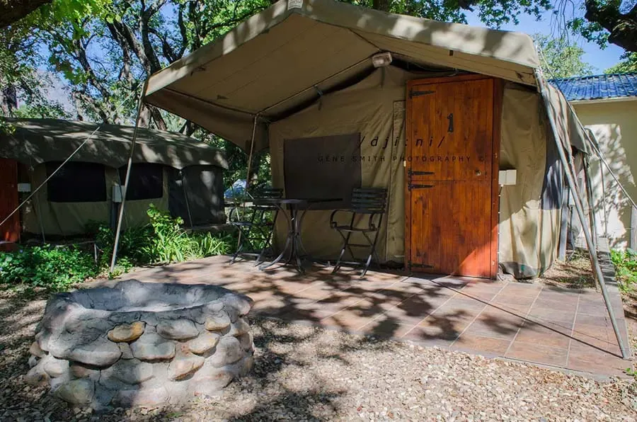 Tent cabin with wooden door outdoor seating and stone fire pit in sunlight
