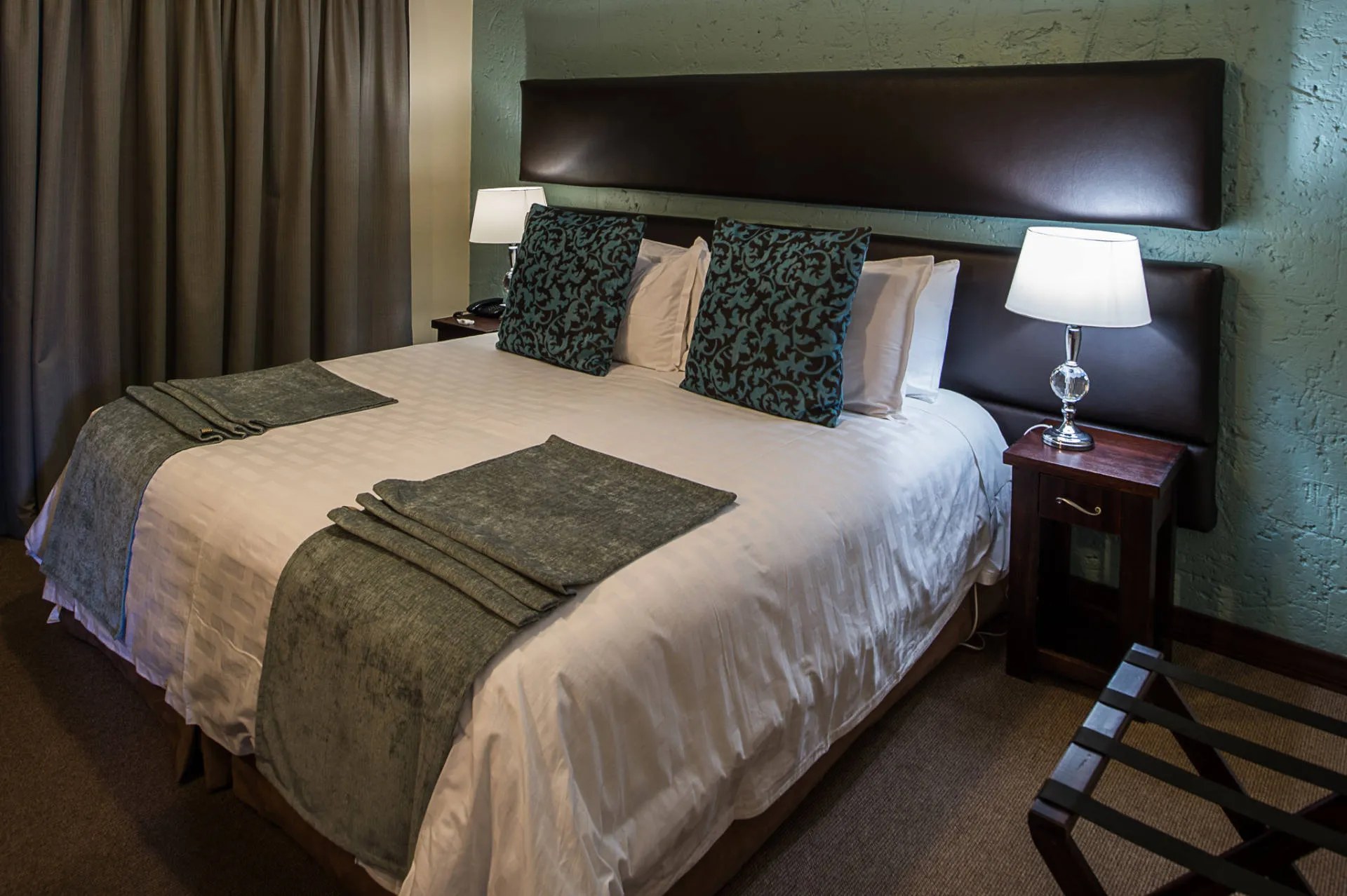 Large bed with green and white bedding in a modern bedroom with lamps