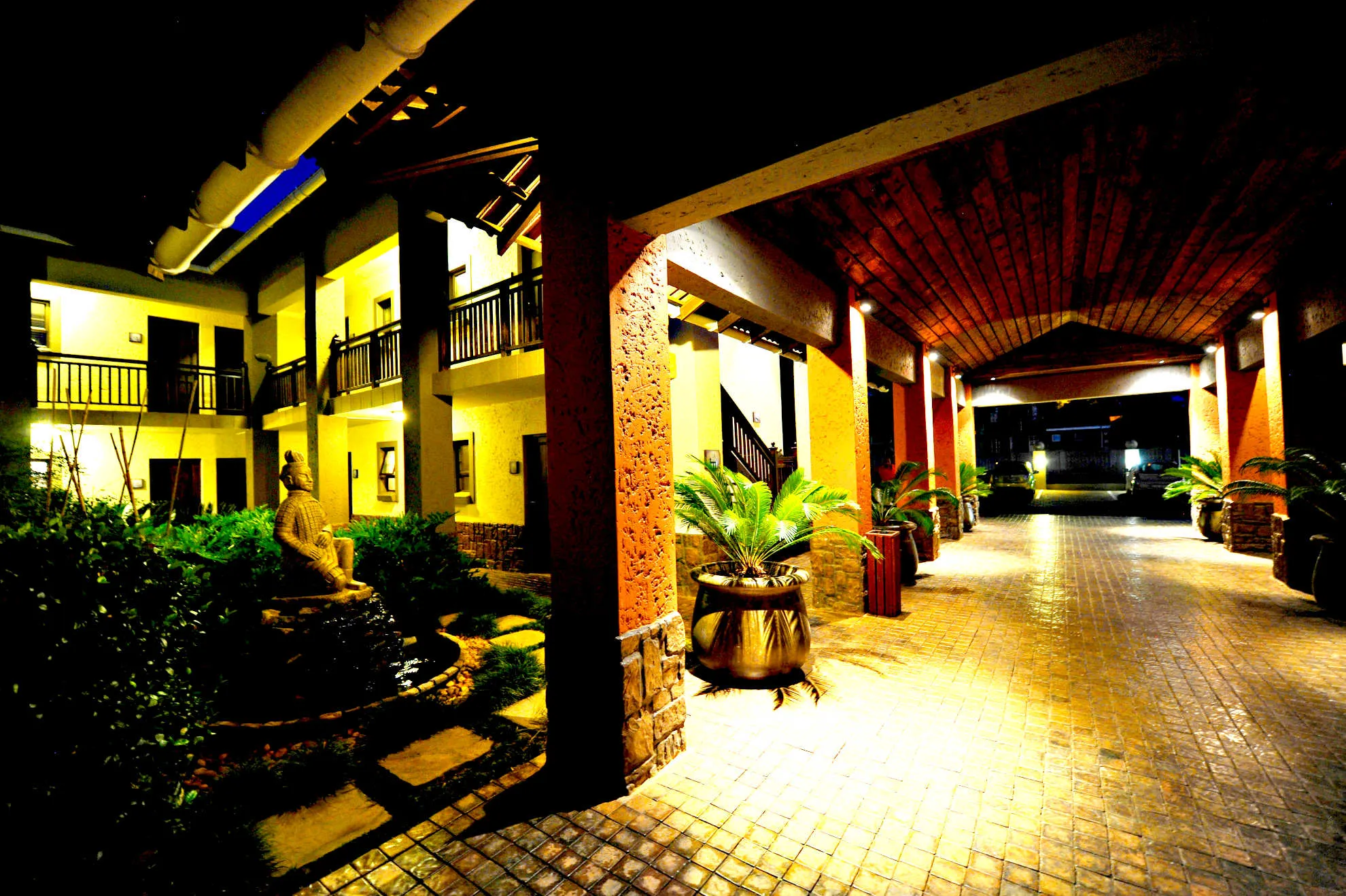Night view of a welllit hotel courtyard with plants and a statue