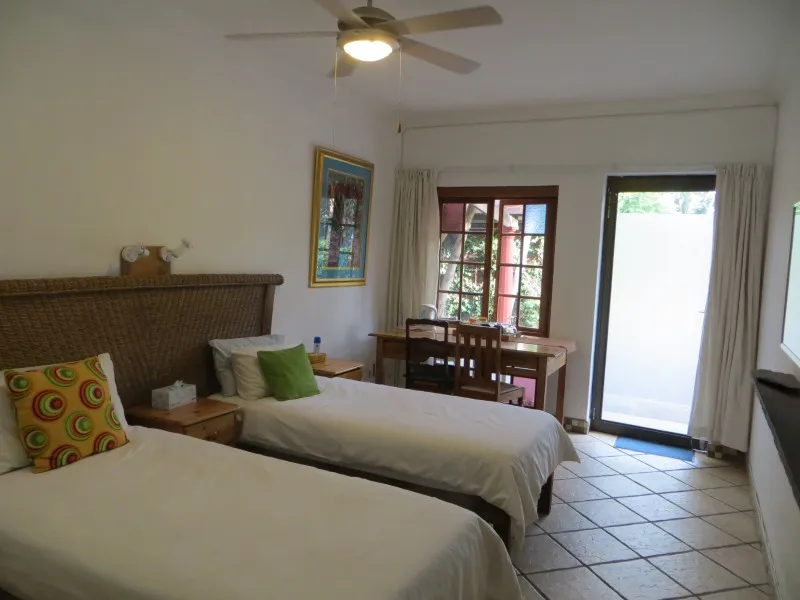 Two single beds in a bright bedroom with a desk and window