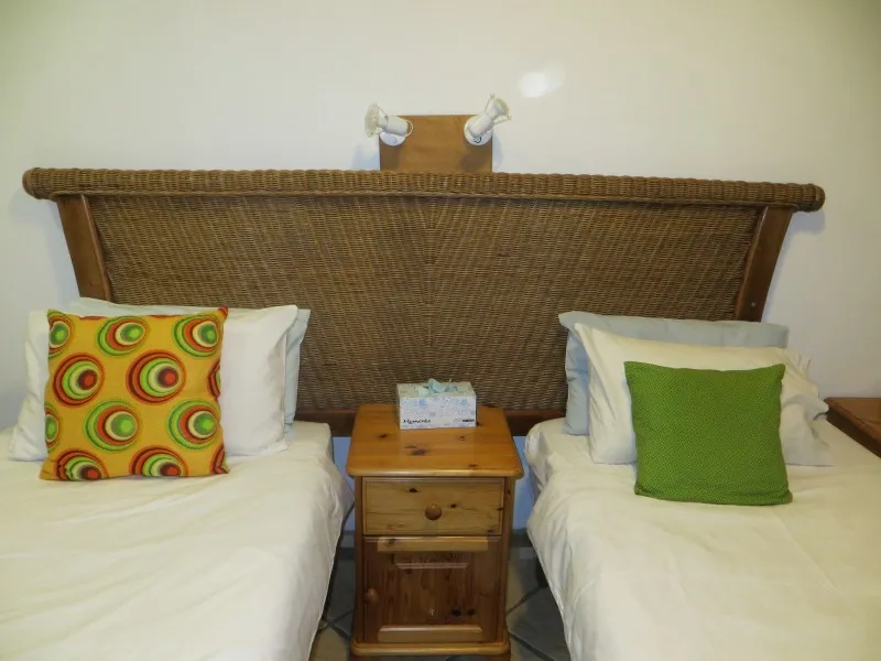 Two single beds with colorful pillows and a wooden nightstand between them