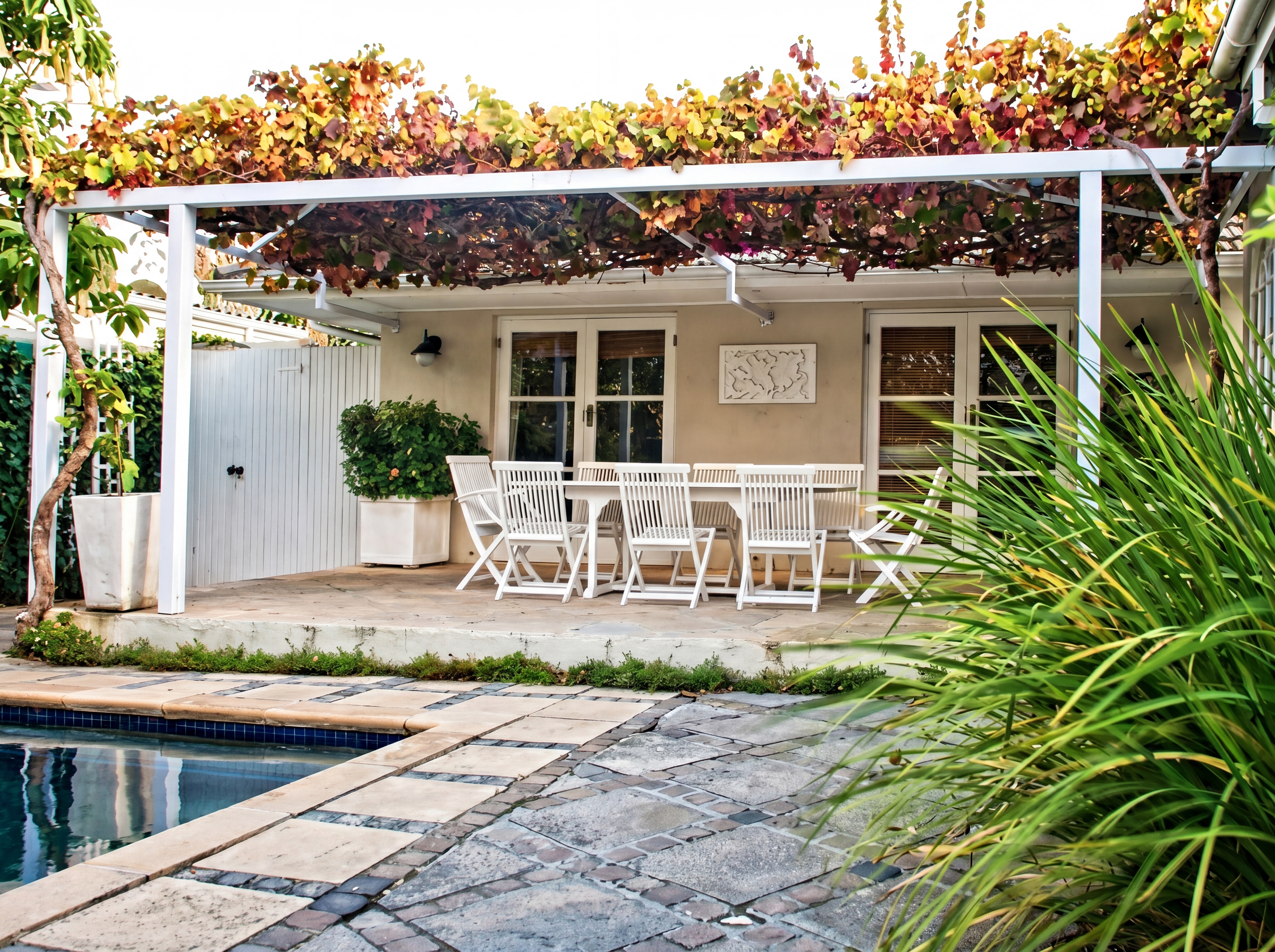 Patio with white furniture pergola and garden beside a pool