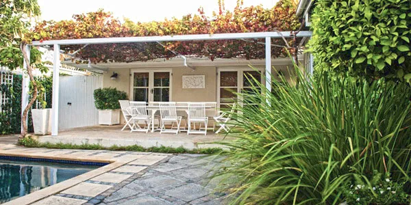 Patio with white furniture pergola and garden beside a pool