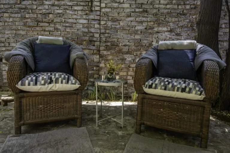 Two wicker chairs with cushions in front of a brick wall