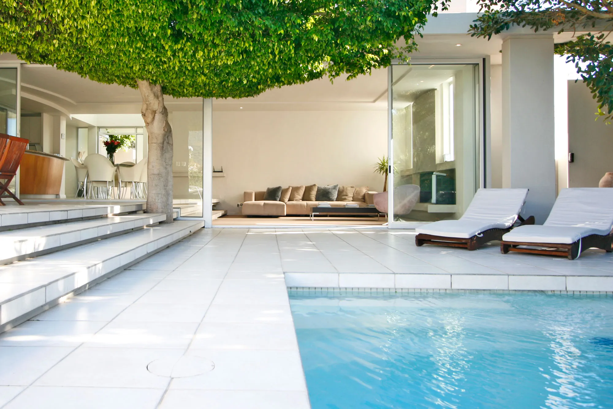 Modern patio with pool lounge chairs and view into a living room