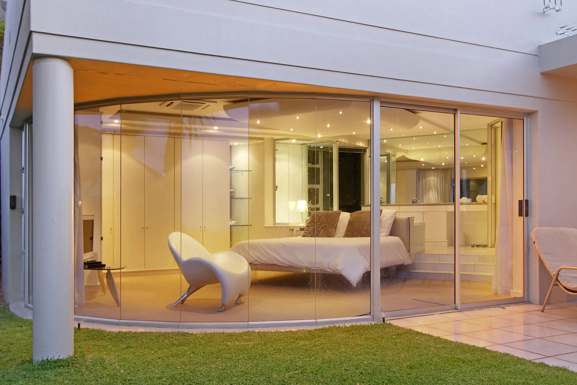 Modern bedroom with large glass walls overlooking a garden at night