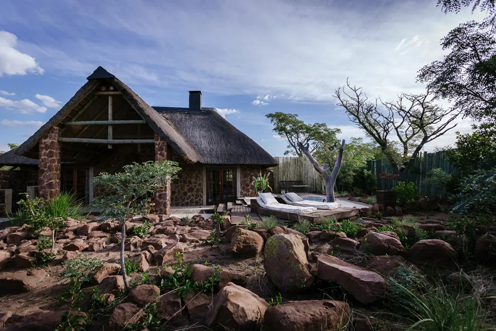 Stone and thatch house with a garden and rock landscaping in a sunny setting