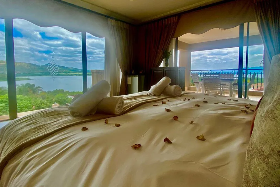 Bed with rose petals towels and a view of a lake and hills