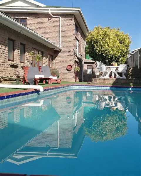 Swimming pool with reflection of house and garden furniture in a sunny backyard