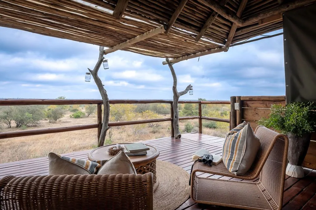 Wooden deck with wicker furniture overlooking a savannah landscape under a cloudy sky
