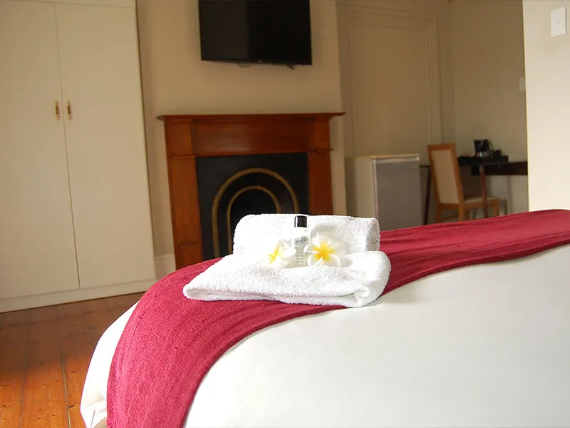 Bed with folded towel flowers and toiletries in a hotel room with fireplace