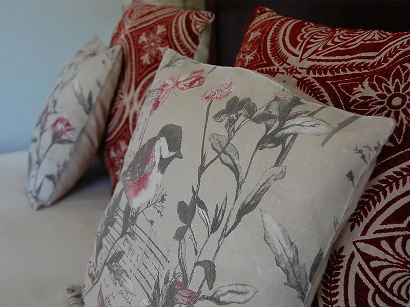 Three decorative pillows with floral and bird patterns on a bed