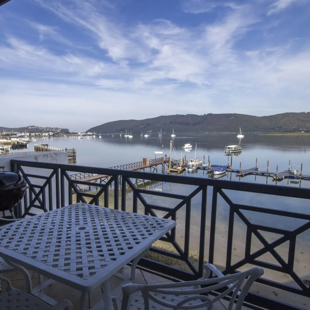 Patio with table and chairs overlooking a marina and mountains