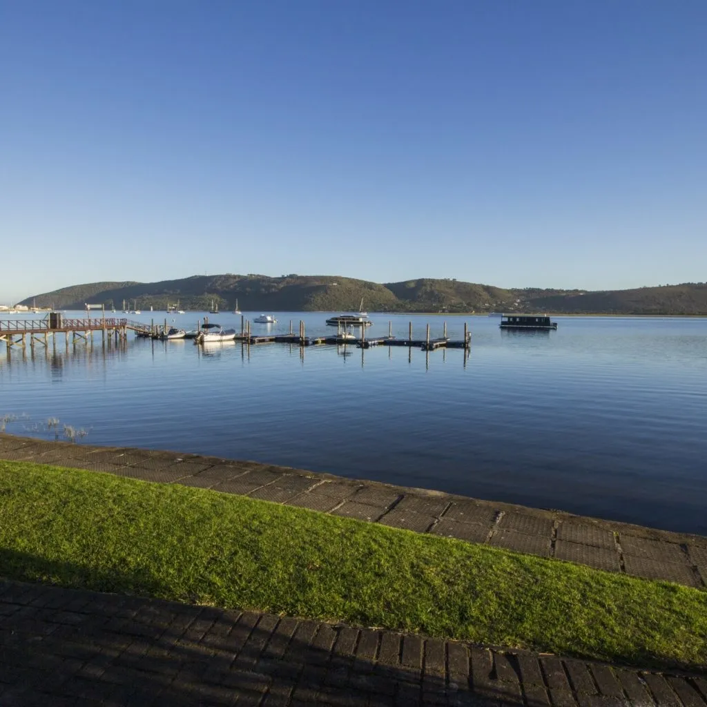 Boats docked at a pier with green grass and a paved path in foreground