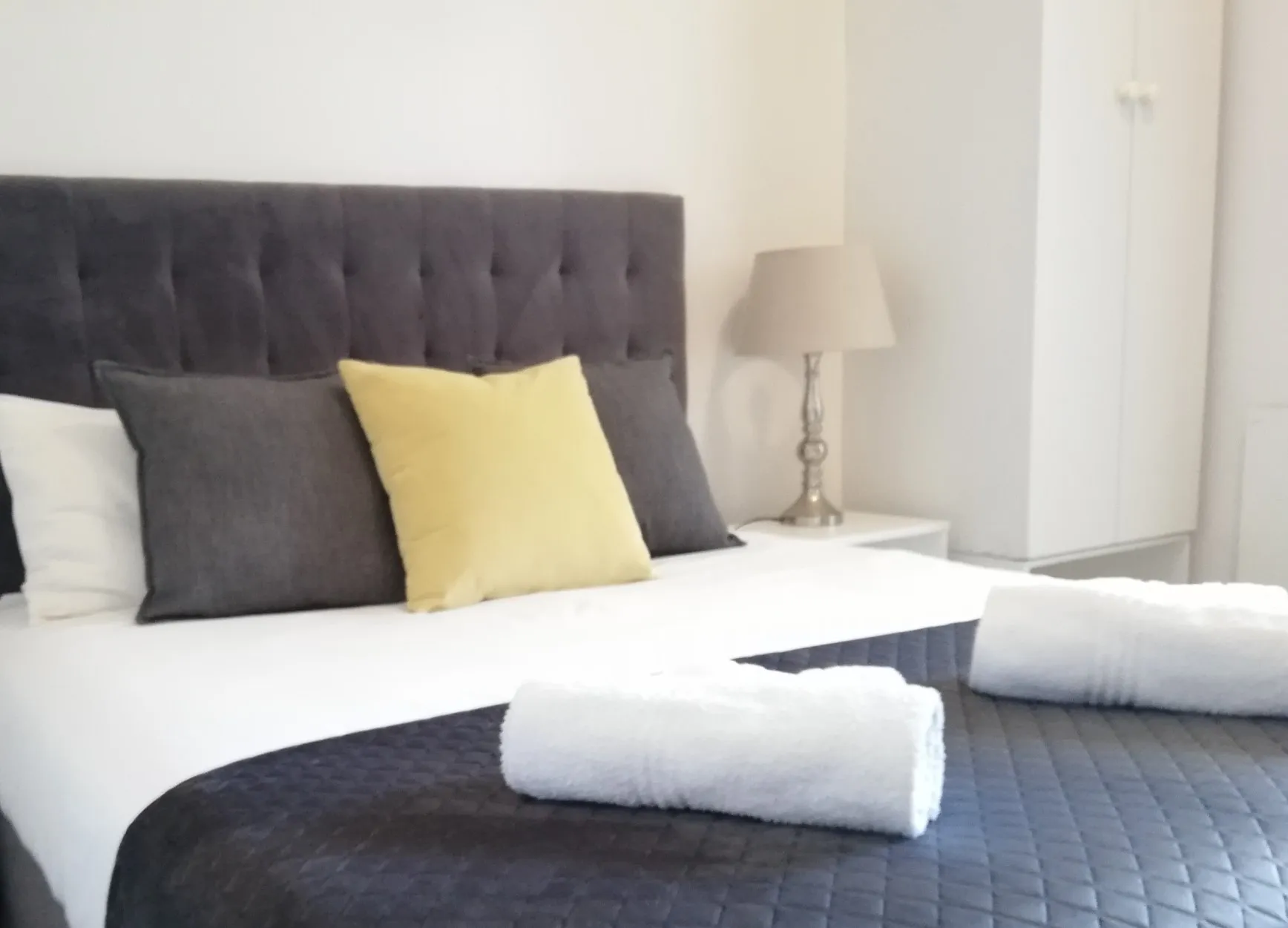 Modern bedroom with neatly made bed pillows and rolled towels on bedspread
