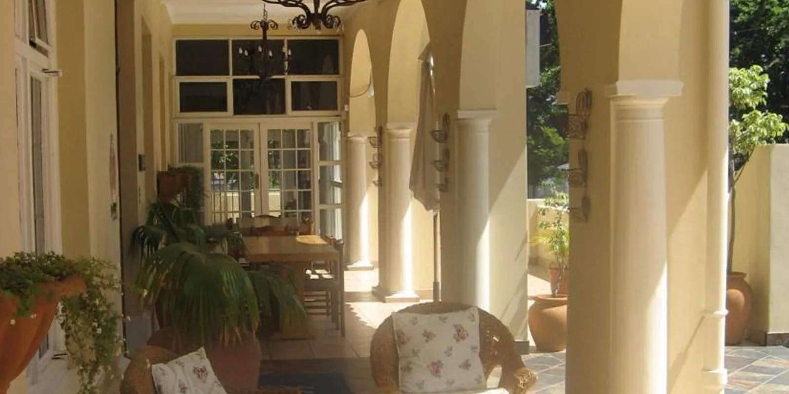 Sunlit patio with wicker chairs plants and arched columns leading to a door