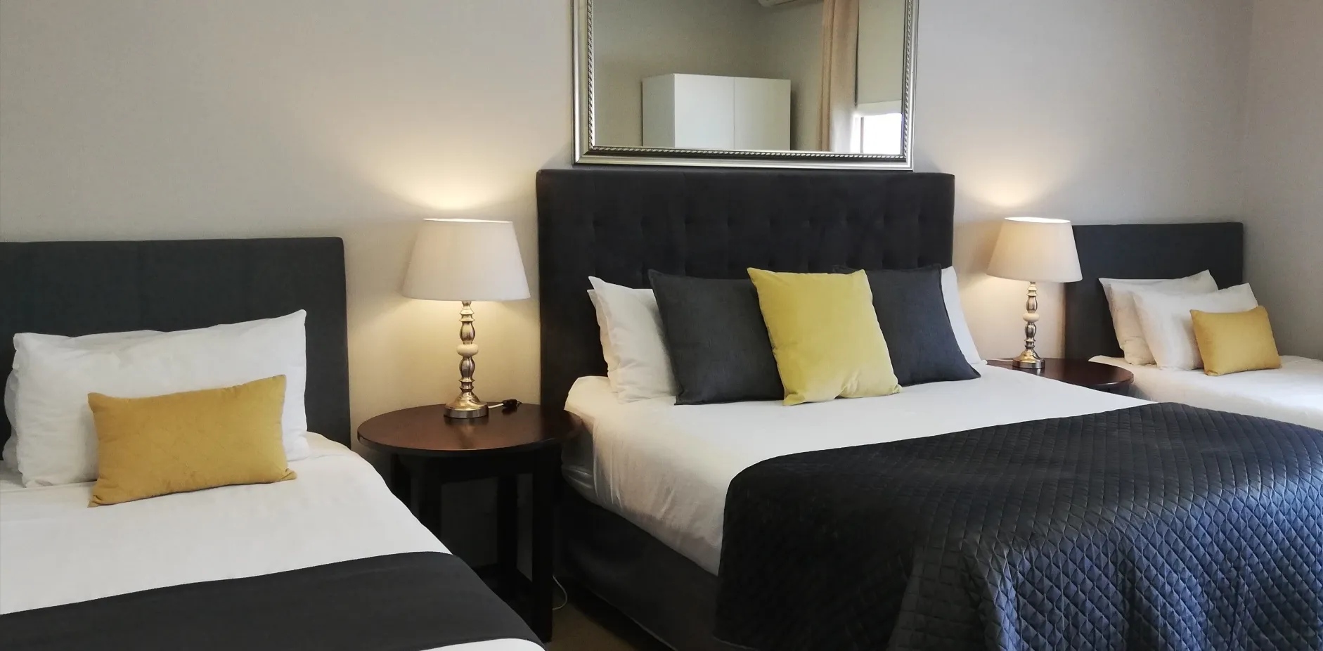 Two beds with black and yellow pillows in a modern bedroom with lamps