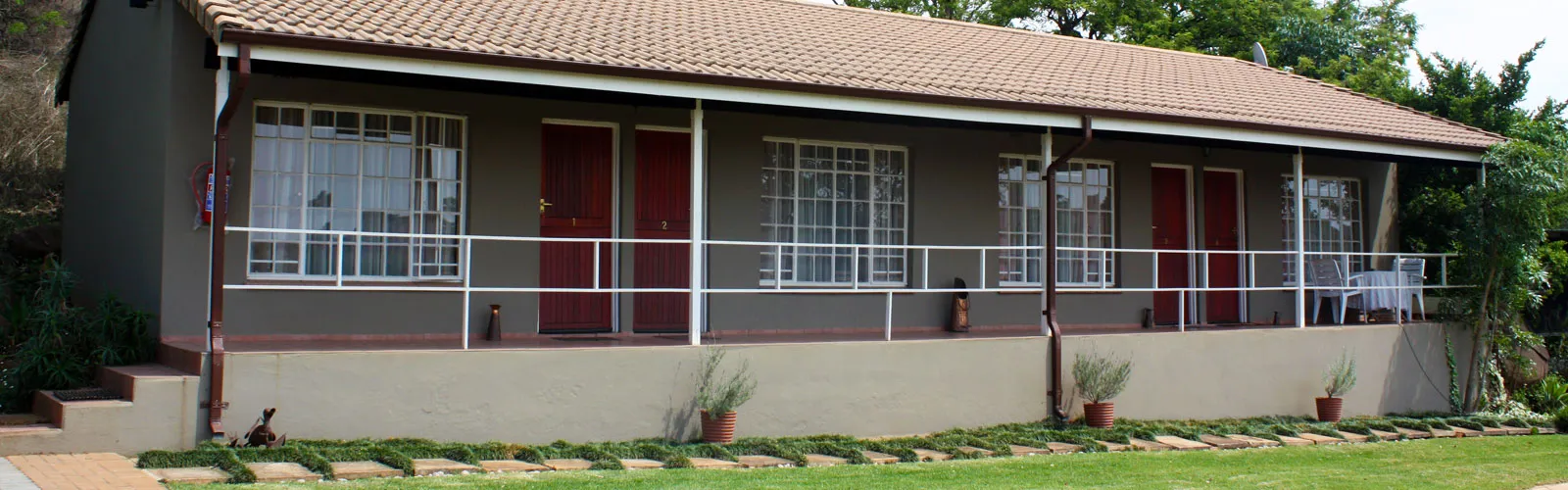 Singlestory building with tiled roof multiple doors windows and potted plants